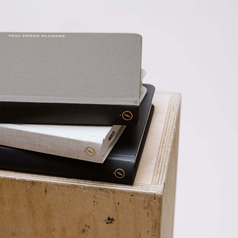 Stack of Full Focus Planner - Linen - Annual Subscription notebooks on a wooden surface showcasing classic design.